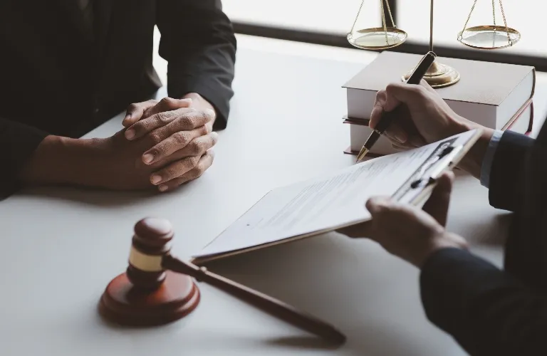 Two individuals at a desk with legal documents, a gavel, and scales of justice.