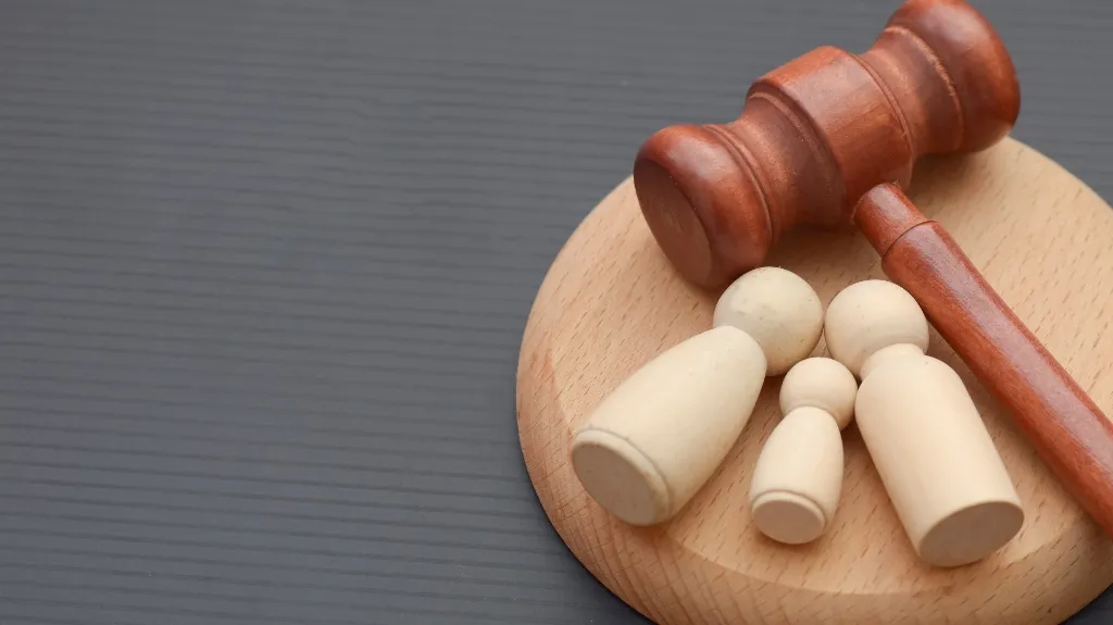 Wooden judge's gavel and base with four beige wooden pawn figures on gray background.