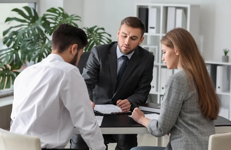 Three business professionals seated around a desk reviewing documents in a modern office.