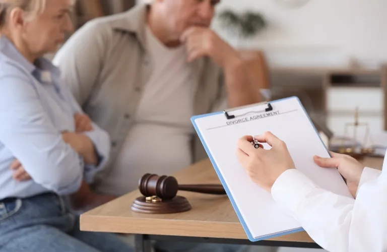 Two individuals seated opposite a professional holding a clipboard labeled "Divorce Agreement" with a judge's gavel on the table.